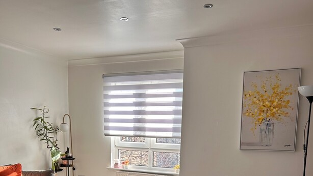 A modern living room with a sofa, a coffee table, a patterned rug, a radiator, a window with blinds, and a floor lamp.