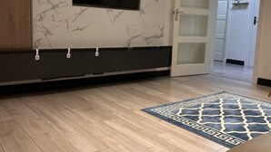 A modern living room with a marble wall, a flat-screen TV, wooden flooring, and a patterned rug.