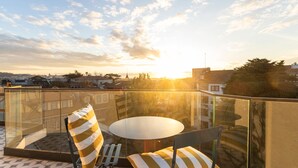 Un balcon doté d’une balustrade en verre, d’une table ronde et de coussins à rayures.