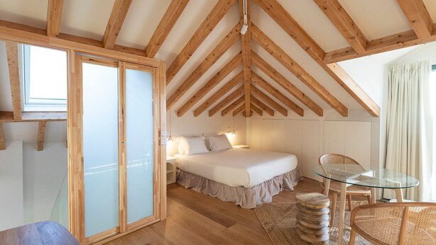 Une chambre avec un plafond en bois, un lit, une table en verre et une chaise.