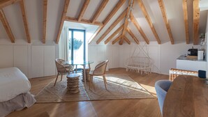 Une chambre mansardée chaleureuse avec un plafond en bois, une table en verre avec des chaises, un fauteuil suspendu et un lit.