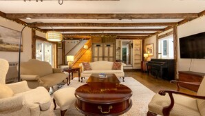 A cozy living room with a sofa, armchairs, a coffee table, and a piano.