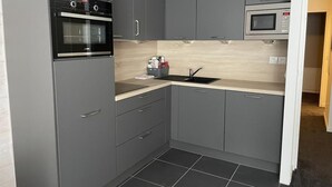 Une cuisine de taille réduite avec des meubles gris, un four noir, un four à micro-ondes et un évier doté d’un plan de travail en bois.