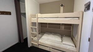 Une chambre avec un lit superposé, une échelle, une petite étagère et une porte.