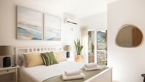 Une chambre à coucher avec un lit, des tables de chevet, une plante en pot et une vue sur l’extérieur.