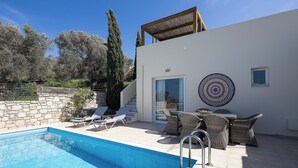 Un espace piscine extérieur moderne, doté de chaises longues, d’une table à manger et d’une décoration murale à motifs.