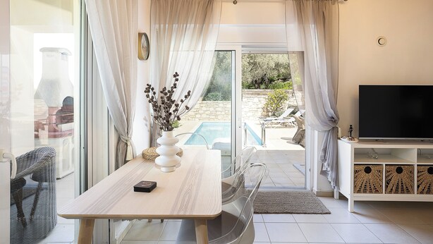 Un salon moderne doté d’une porte vitrée donnant sur une piscine, d’un téléviseur à écran plat et d’une table à manger agrémentée d’un vase de fleurs séchées.