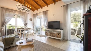 Un salon spacieux avec un plafond en bois, une télévision, un canapé, une table basse et un coin repas comprenant des chaises et une table.