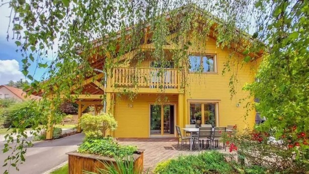 Ein gelbes, zweistöckiges Haus mit Balkon, einer Terrasse und Gartenmöbeln sowie einem Gartenbereich.