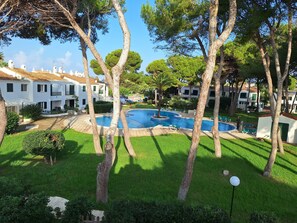 A pool area surrounded by white buildings with balconies, a well-maintained lawn, and trees.