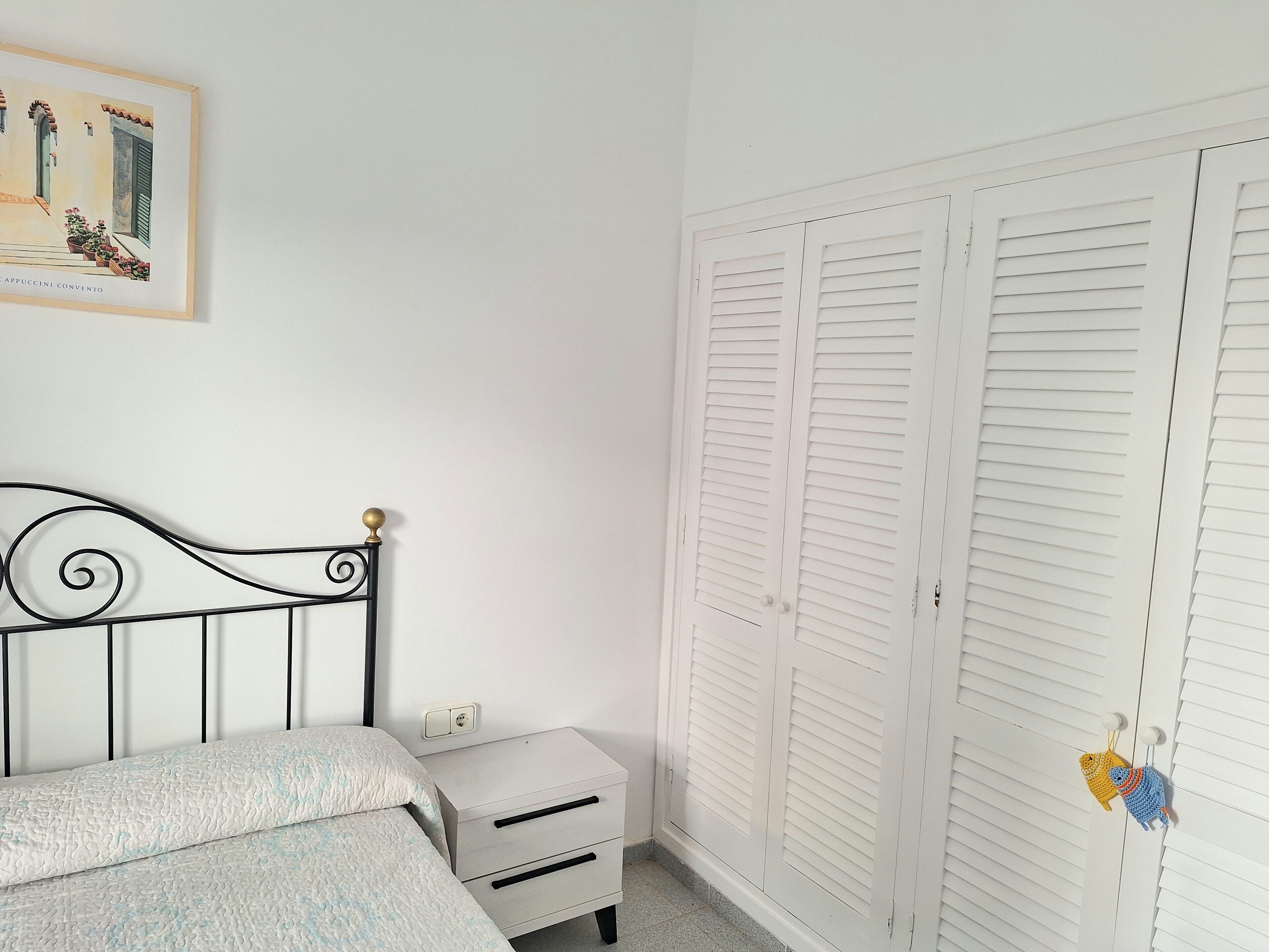 Ein Schlafzimmer mit einem Bett, einem Nachttisch, einem Kleiderschrank und einem gerahmten Bild an der Wand.