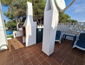 A patio with a barbecue grill, a table, chairs, and a view of a swimming pool.