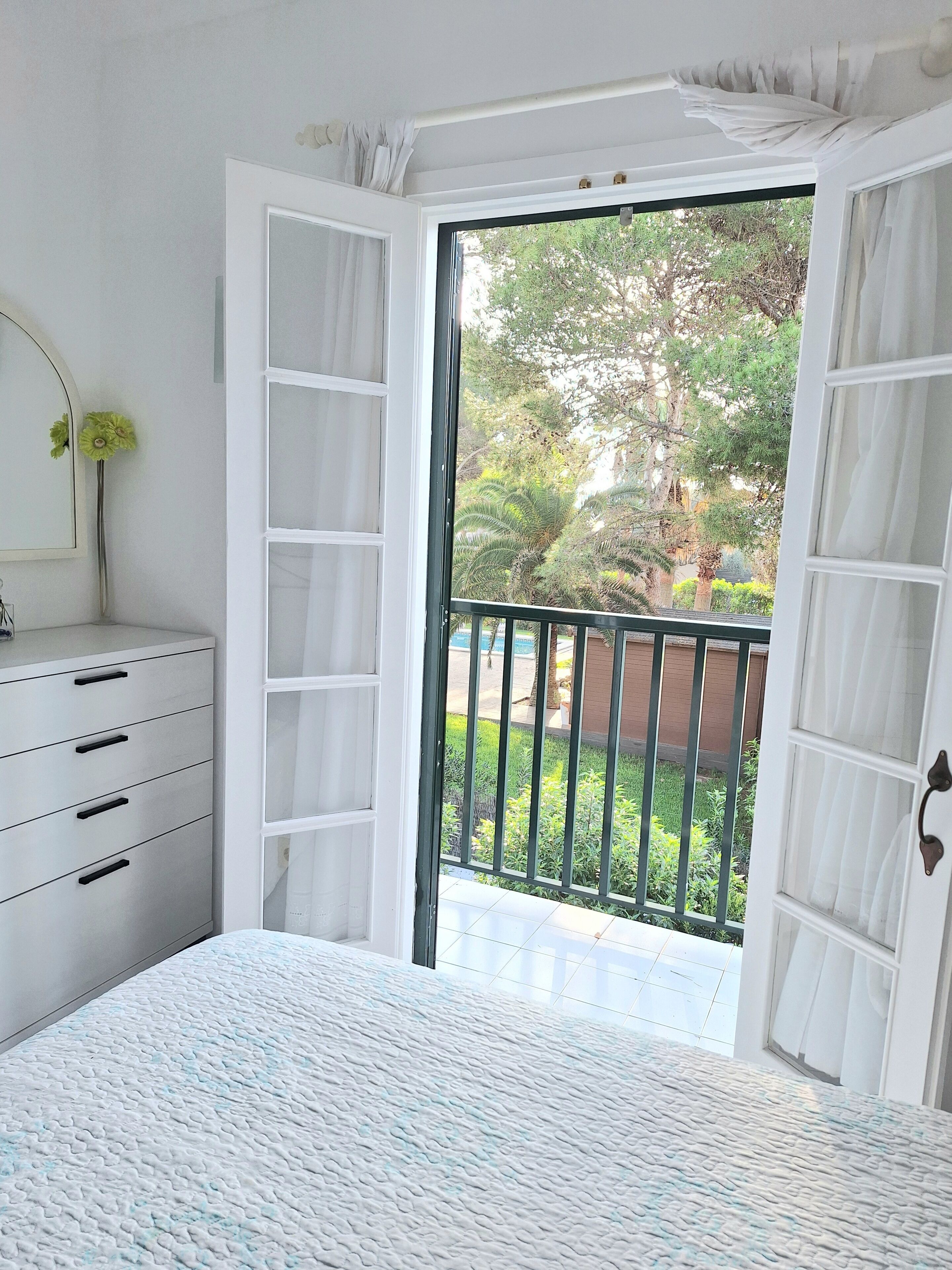 Une chambre à coucher avec un lit, une commode et une fenêtre donnant sur un paysage verdoyant.