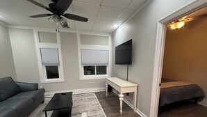 Un ambiente compatto con ventilatore a soffitto, TV a parete, divano, tavolino e un letto.