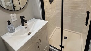 Un bagno moderno con un lavandino bianco, un rubinetto nero e un box doccia in vetro.