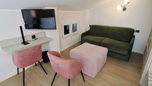 A modern living room with a flat-screen TV, a green sofa, a pink chair, and a pink ottoman. - Hotel Miratorre (Pisa)