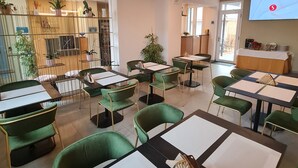 A modern dining area with green chairs and tables, a TV screen, and a decorative wall with plants. - Hotel Miratorre (Pisa)