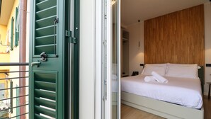A bedroom with a bed, a wooden wall, and a balcony with green shutters. - Hotel Miratorre (Pisa)