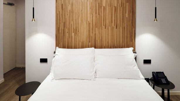 A hotel room with a wooden headboard, white bedding, a black bedside table with a phone, and pendant lighting. - Hotel Miratorre (Pisa)
