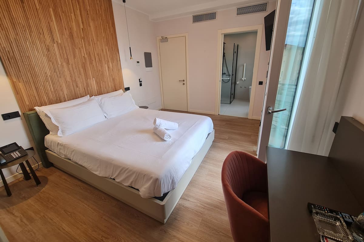 A hotel room with a large bed, a desk, a chair, and a shower area.