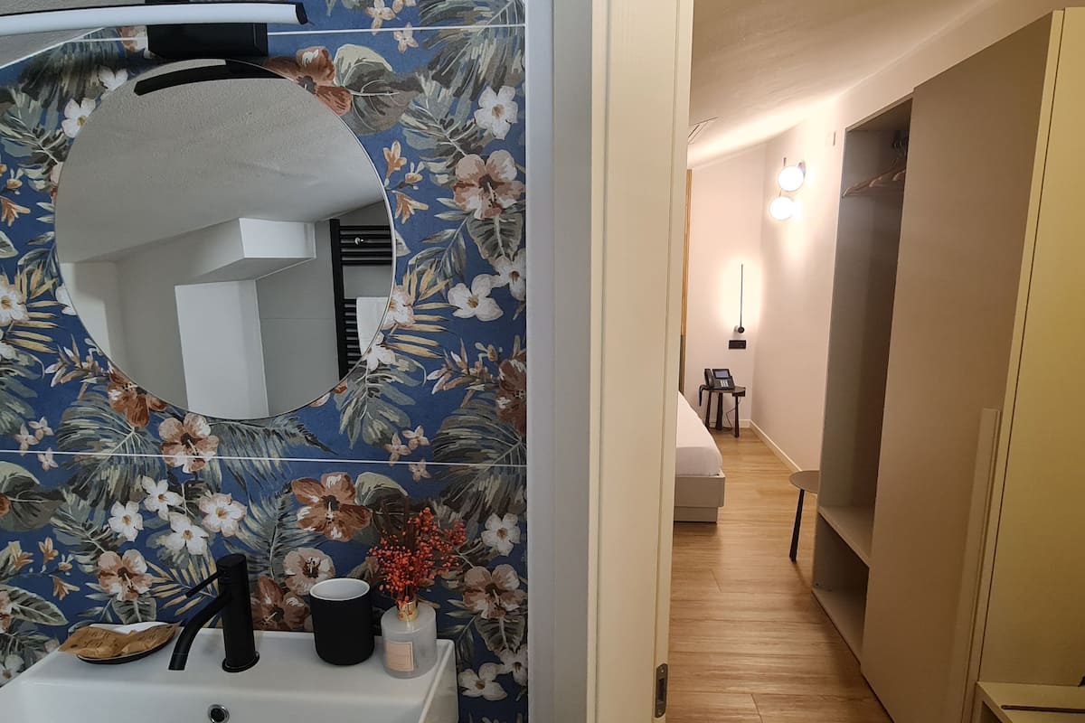 A bathroom with a floral tile backsplash, a round mirror, a sink, and a small table with a cup and decorative item.