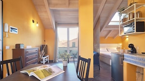 A cozy room with a wooden ceiling, a dining table with a magazine, a small kitchen area with a refrigerator, and a balcony with a view. - Tra le Torri (Albenga)