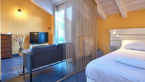 A modern bedroom with a large bed, a sofa, a television, and a wooden ceiling. - Tra le Torri (Albenga)