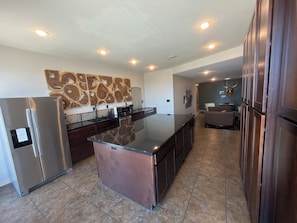 A modern kitchen with stainless steel appliances, a marble countertop island, and recessed ceiling lighting.