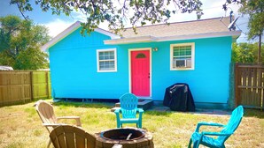 A blue house with a red door, a fire pit, and two Adirondack chairs.