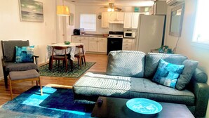 A living room with a grey sofa, a small table, a chair, and a kitchen in the background.