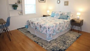 A bedroom with a bed, bedside tables, a chair, a desk, shelves, and a window.