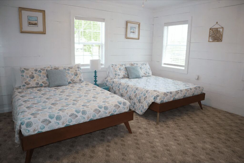 Een slaapkamer met twee bedden, elk met een gebedrukte spreidek en passende kussens. Er hangen ingelijste foto’s aan de muur en op het nachtkastje staat een klein decoratief object.
