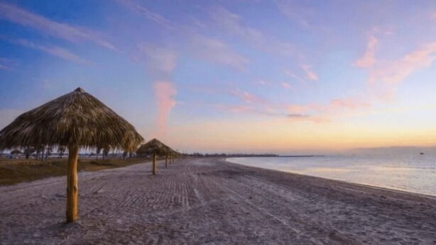 A beach with a thatched umbrella and a clear sky.