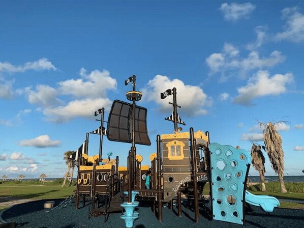 A playground with various play structures including a pirate ship, a castle, and slides.