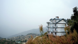 A multi-story building with balconies, situated on a hillside with a view of the surrounding landscape. - Aagaman- Your Mountain Home (Naldehra)