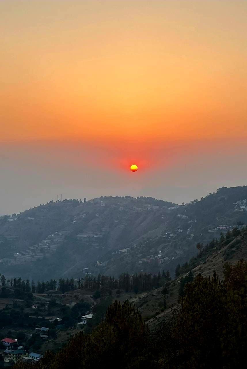 A sunset over a hilly landscape with scattered buildings.