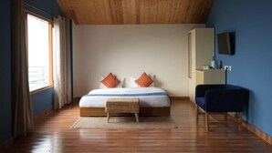 A bedroom with a wooden ceiling, a large bed with two pillows, a small bench, a chair, and a dresser with a mirror. - Aagaman- Your Mountain Home (Naldehra)