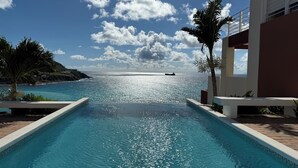 A swimming pool leading to a beach with a ship in the distance, surrounded by palm trees and a clear sky. - Villa España. Beautiful apartment overlooking a spectacular beach (Indigo Bay)