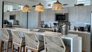 A modern kitchen with a central island, bar stools, hanging pendant lights, and a large window. - Villa España. Beautiful apartment overlooking a spectacular beach (Indigo Bay)