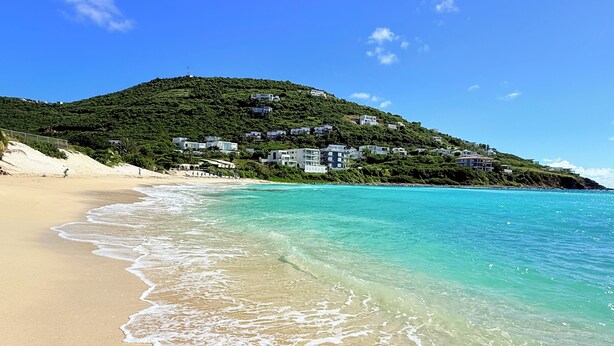 A beach with clear turquoise water, a sandy shore, and a hillside with buildings. - Villa España. Beautiful apartment overlooking a spectacular beach (Indigo Bay)