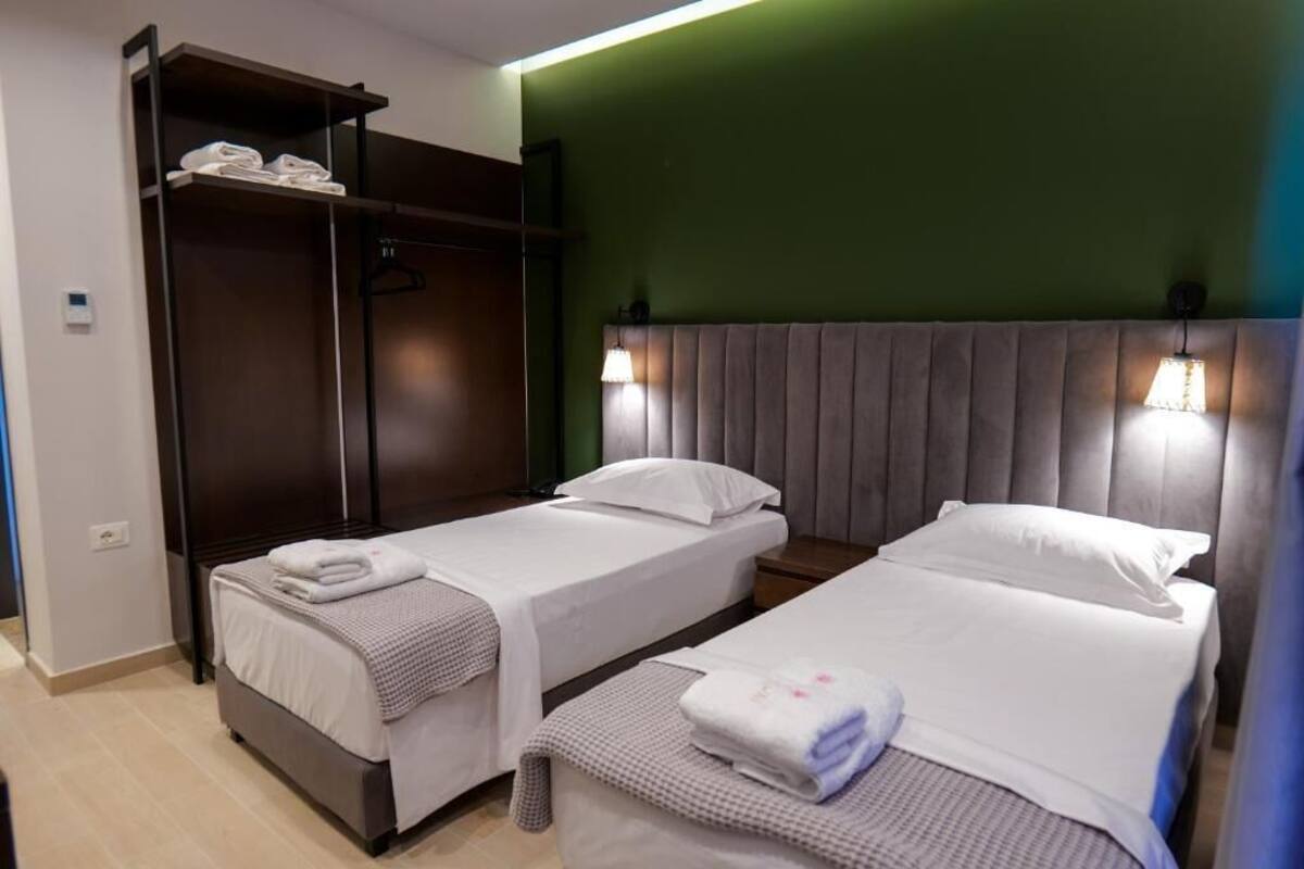 Habitación de hotel con dos camas individuales, un armario y una pared de acento verde.