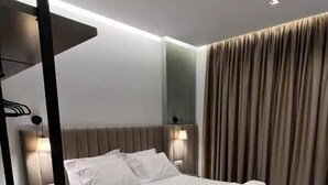A modern hotel room with a large bed, a bedside table, a lamp, and a curtain. - Nerium Hotel (Ksamil)