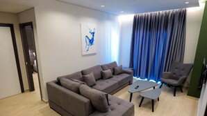 A modern living room with a sectional sofa, a small coffee table, and a grey armchair. - Nerium Hotel (Ksamil)