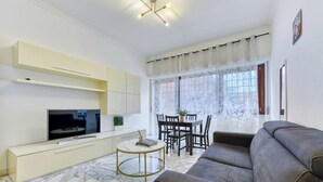 Un salon comprenant un canapé, un téléviseur, une table à manger avec des chaises et une fenêtre avec des rideaux.