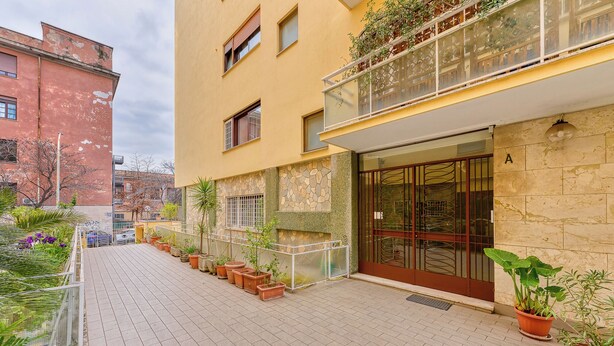 Un immeuble doté d’une façade en pierre, d’un balcon orné de plantes et d’une entrée fermée par un portail.