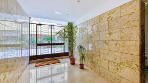 Un hall d’entrée spacieux avec une porte vitrée donnant sur un espace extérieur, des murs carrelés et des plantes en pot.