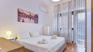Une chambre d’hôtel comprenant un lit, une table de chevet, un bureau, une chaise, une fenêtre avec des rideaux et un climatiseur fixé au mur.