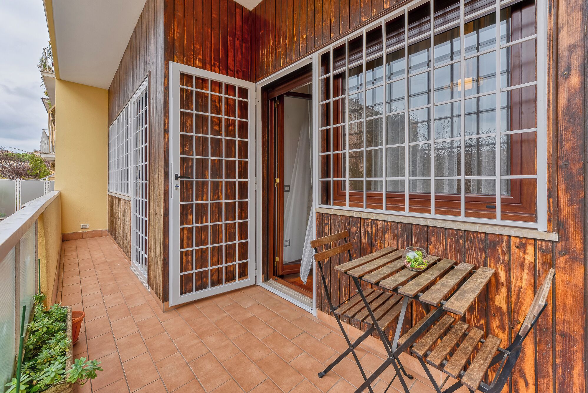 Un balcon doté d’une façade en bois, d’une porte-fenêtre coulissante et d’une petite table en bois.