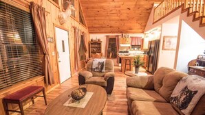 En hyggelig stue med træloft, sofa, sofabord og et spiseområde med et køkken i baggrunden.
