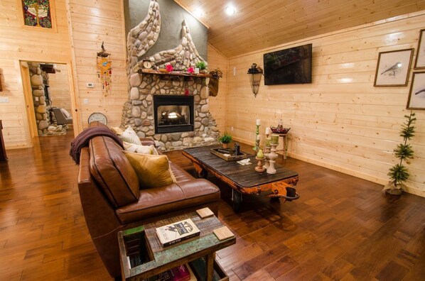 A cozy living room with a stone fireplace, wooden walls, and a leather sofa.